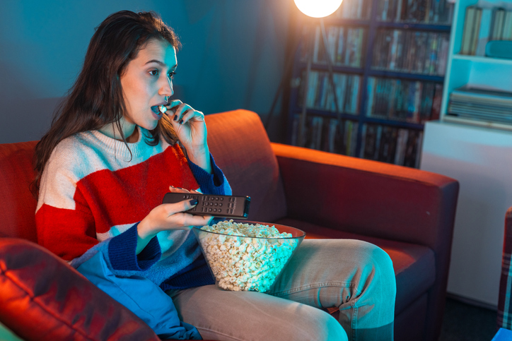 Woman sat on sofa eating popcorn without focusing mindful eating intuitive eating