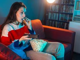 Woman sat on sofa eating popcorn without focusing mindful eating intuitive eating